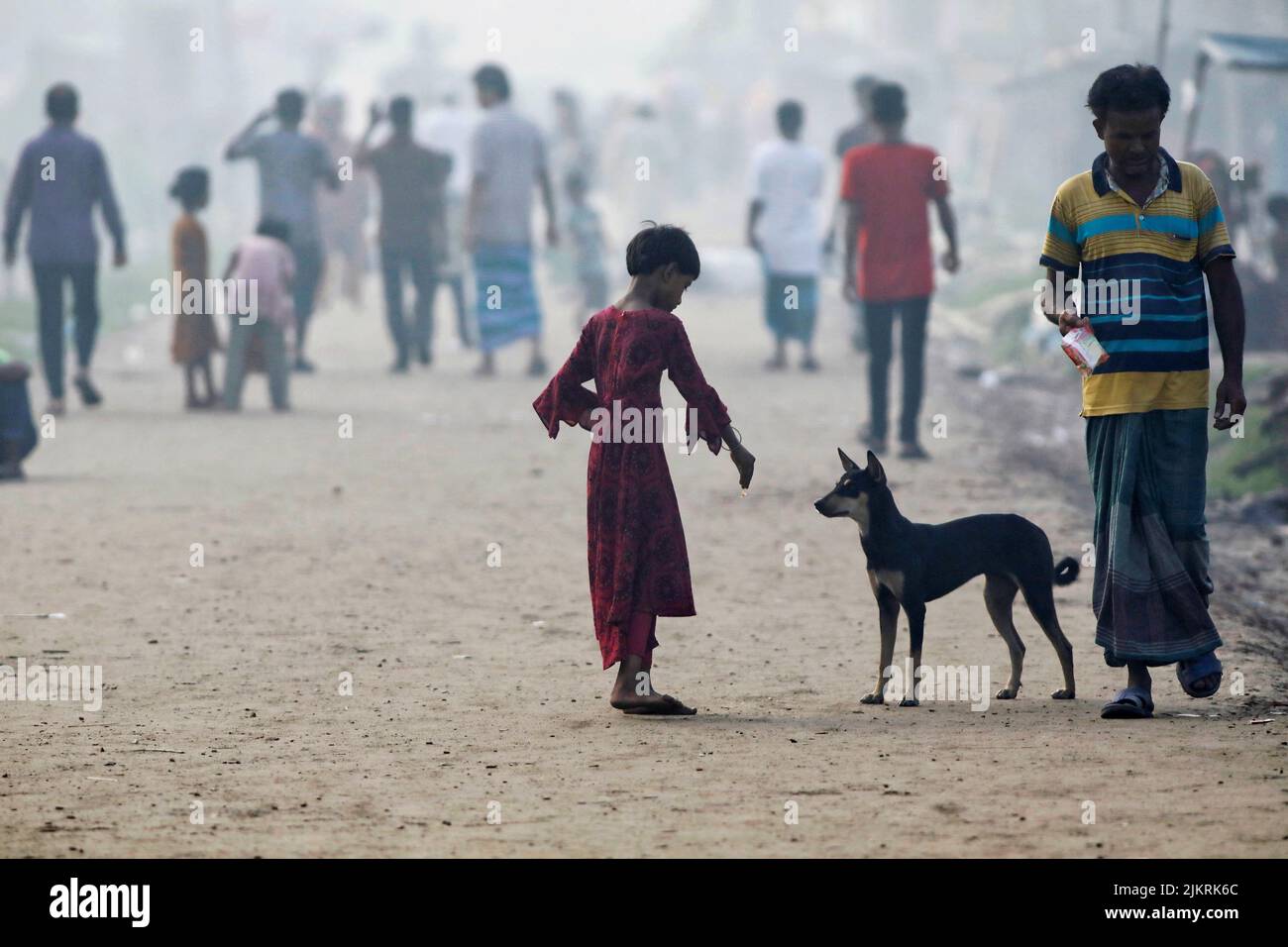 A girl feeds a dog beside an industrial area in Dhaka, Bangladesh, August 3, 2022. REUTERS/Mohammad Ponir Hossain Stock Photo