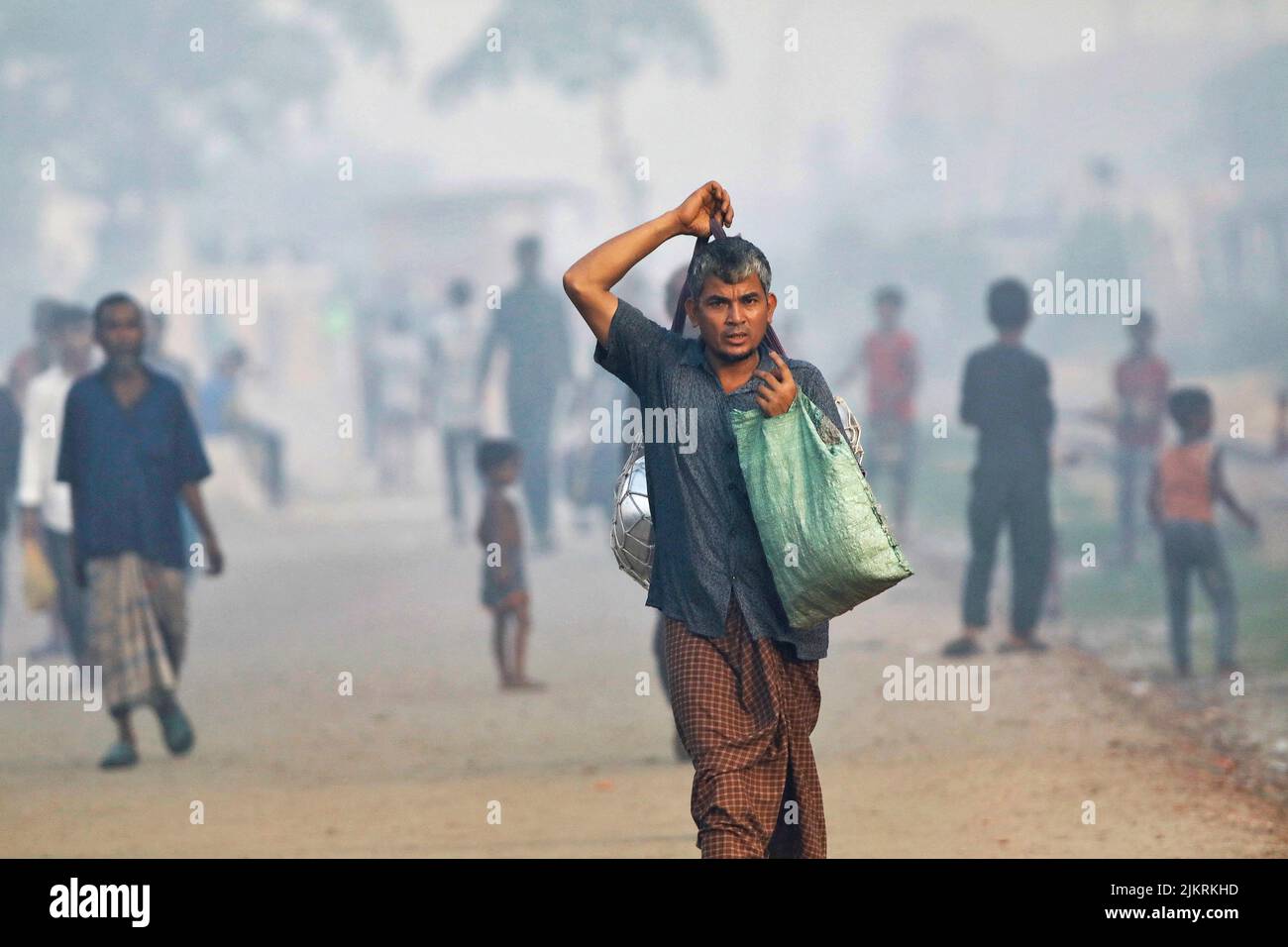 A man walks along a road beside a smoky industrial area in Dhaka, Bangladesh, August 3, 2022. REUTERS/Mohammad Ponir Hossain Stock Photo