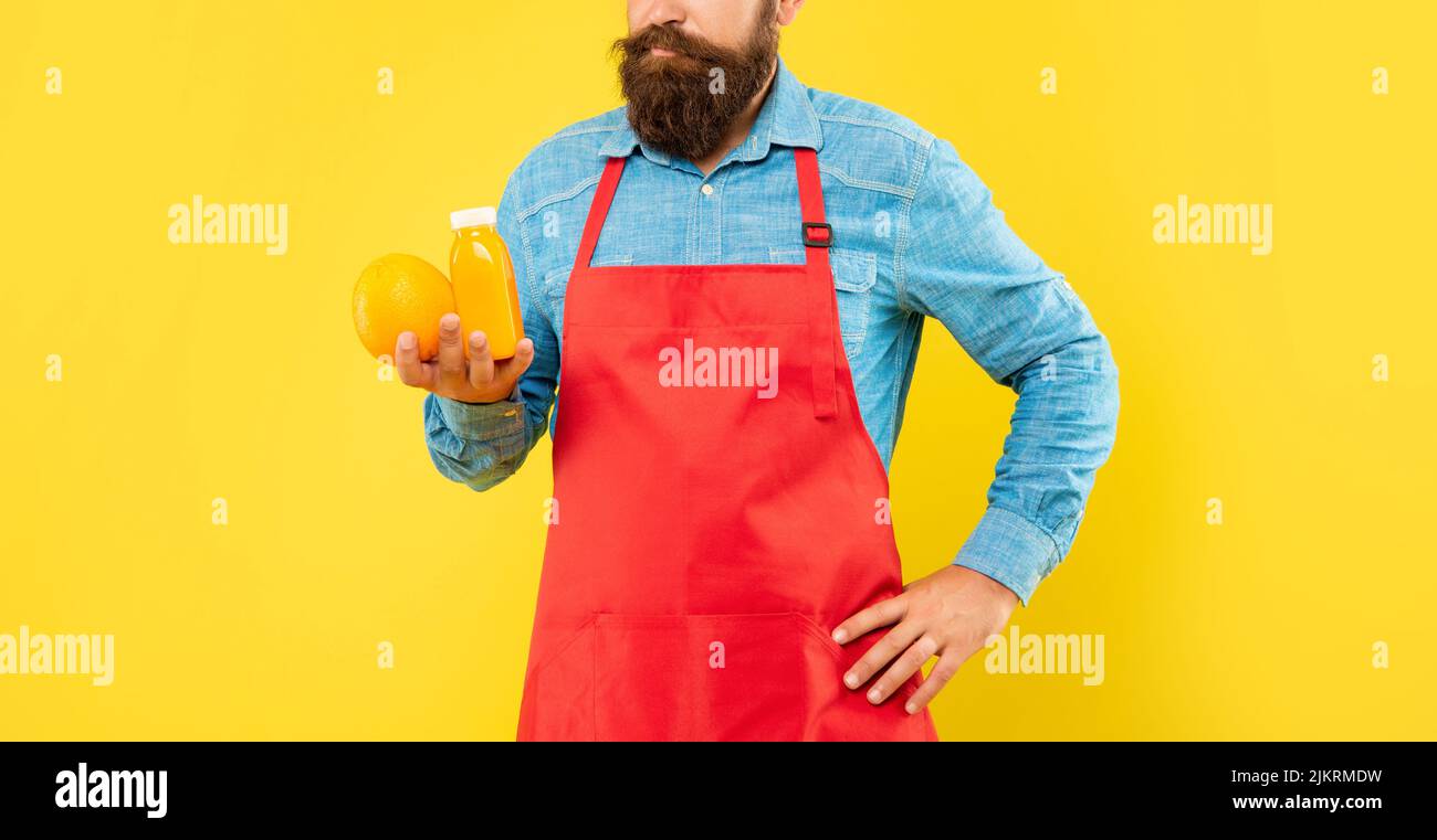Man crop view in apron holding orange and juice bottle yellow background, juicery Stock Photo