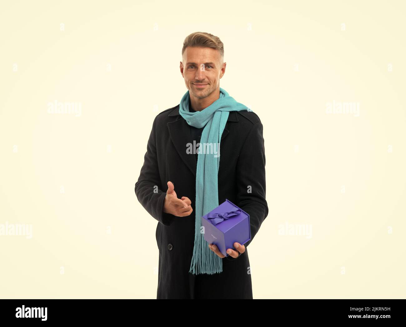 Happy handsome man in overcoat with long scarf pointing finger at gift box, present Stock Photo