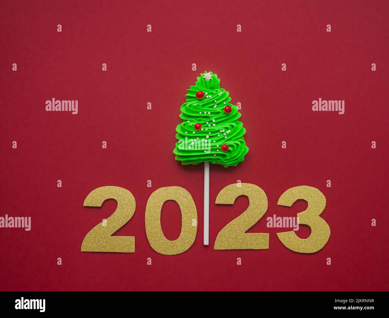 2023 and green candy in the form of a Christmas tree on a red background Stock Photo