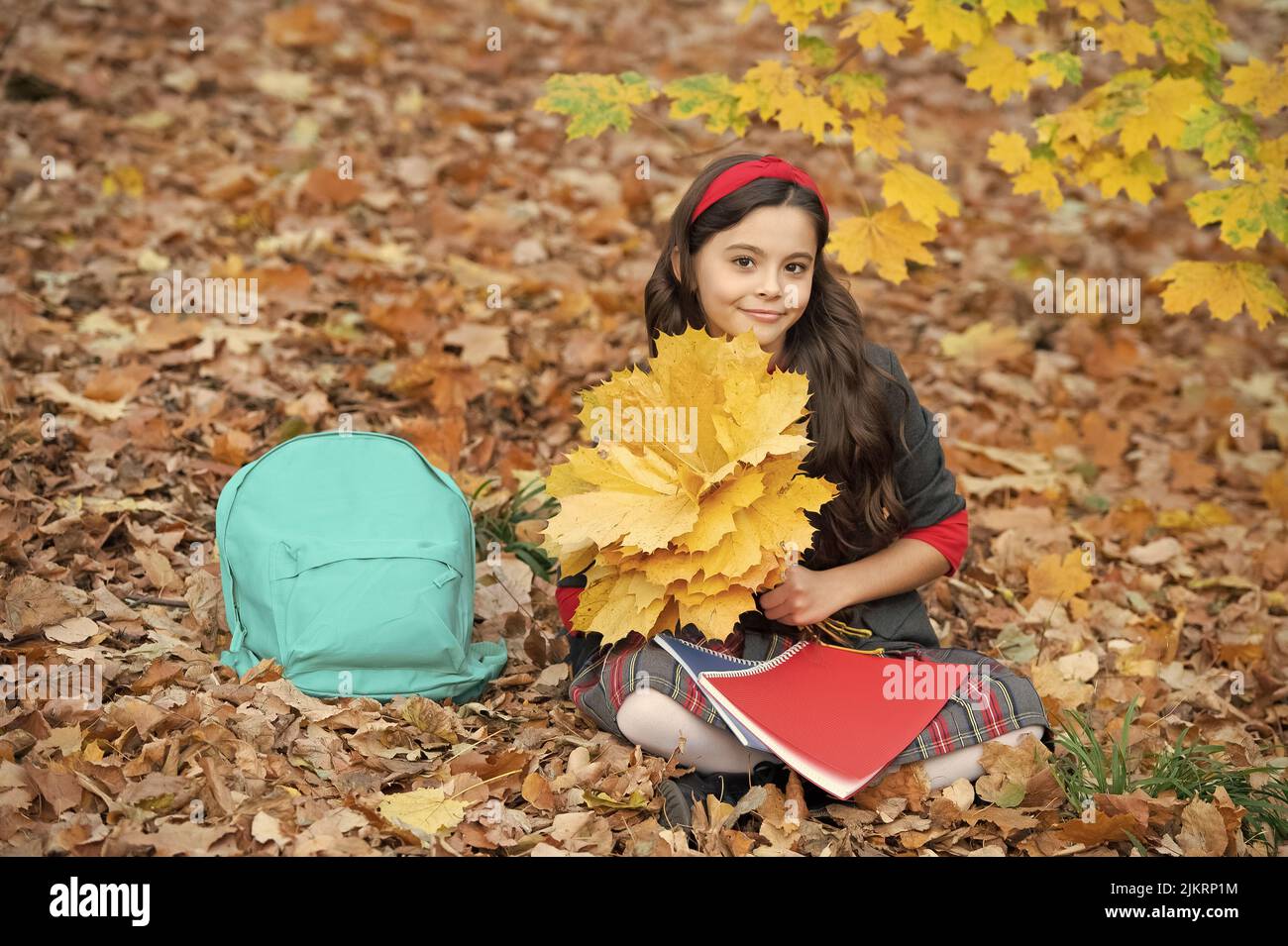 smiling teen girl hold autumn maple leaves with school bag and workbook outdoor, school Stock Photo