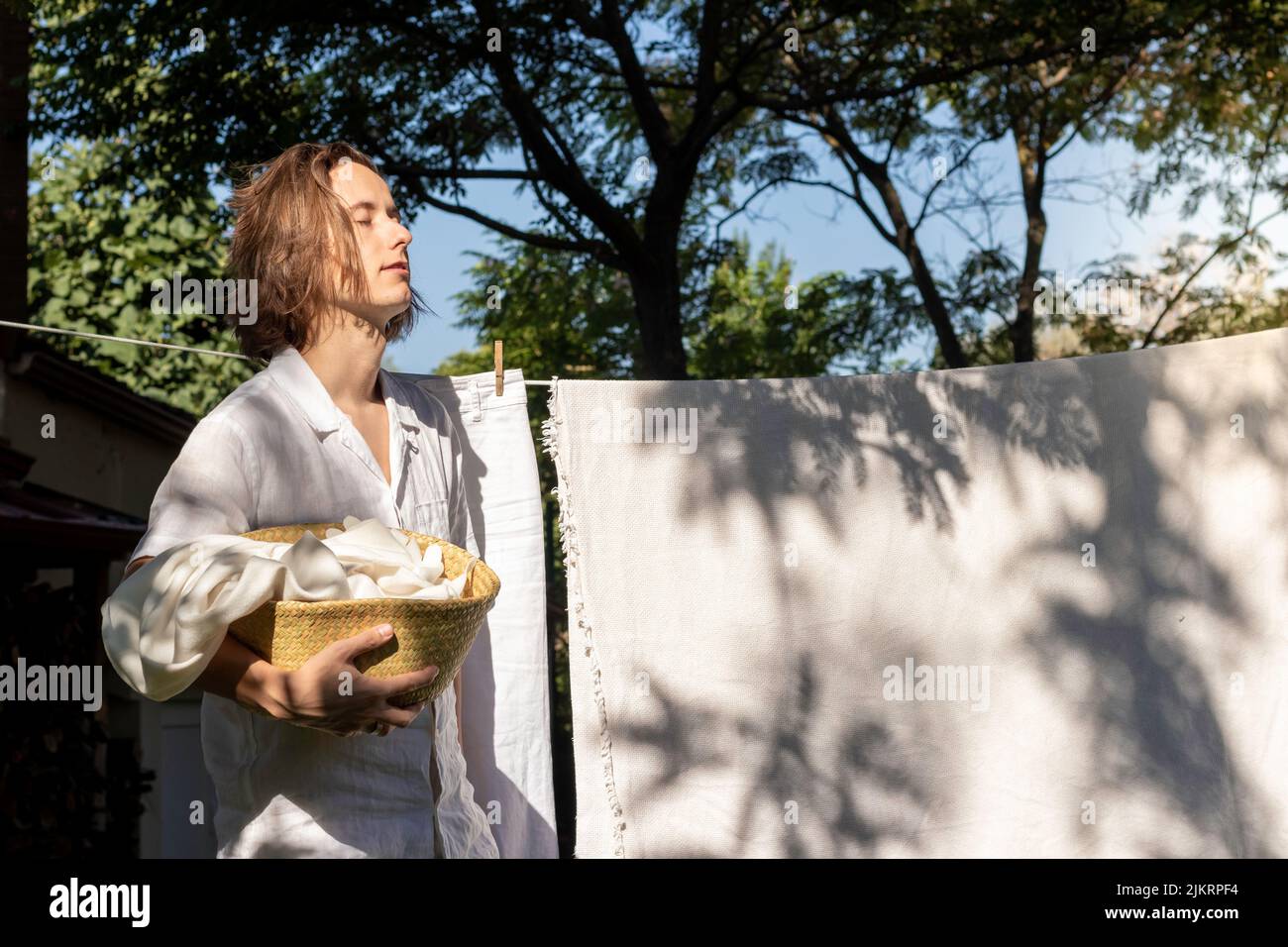 Young long hair man with closed eyes ejoying the summer sun on his face while hanging out the linen washing Stock Photo