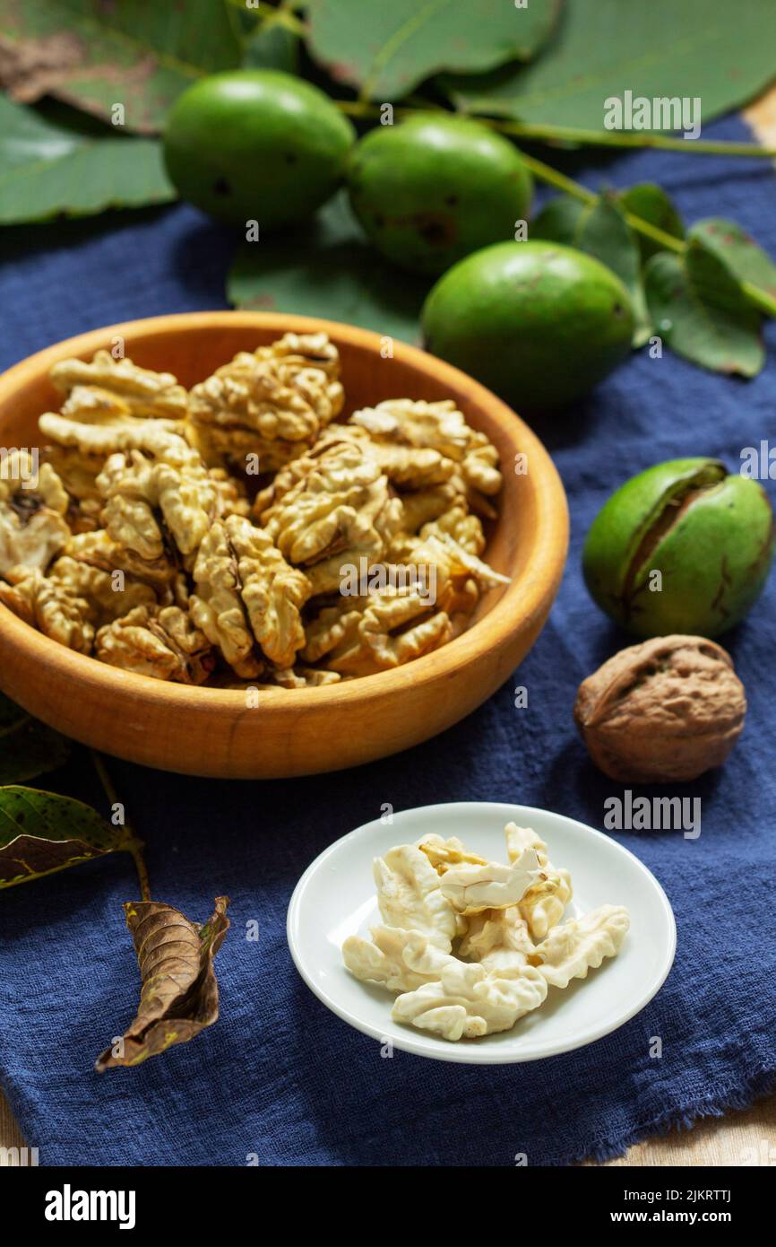 Young walnuts, shelled and in shell, walnut leaves. Rustic style. Stock Photo