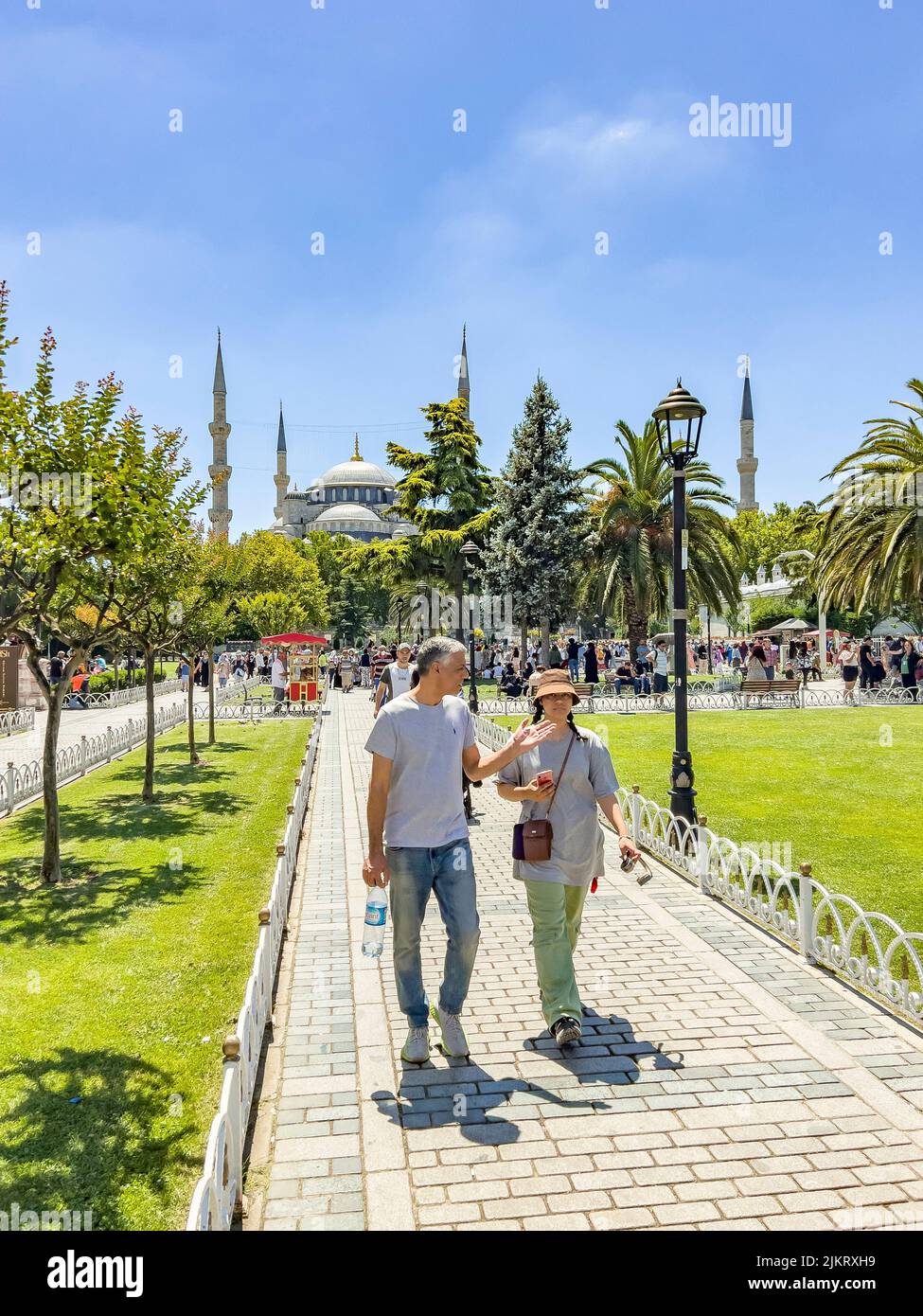 Istanbul - Turkey - July 14, 2022: Casual tourist couple walking in front of the famous blue mosque. Beautiful green public park with green palm trees Stock Photo