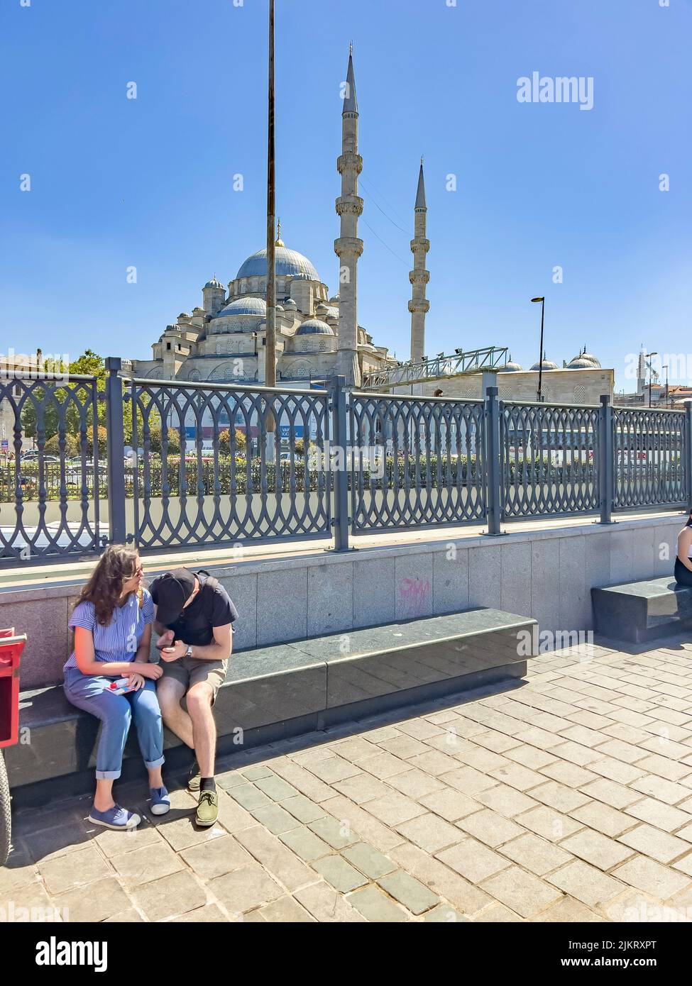 Tourist couple sitting at a bench in front of Yeni Cami, New Mosque, at ...