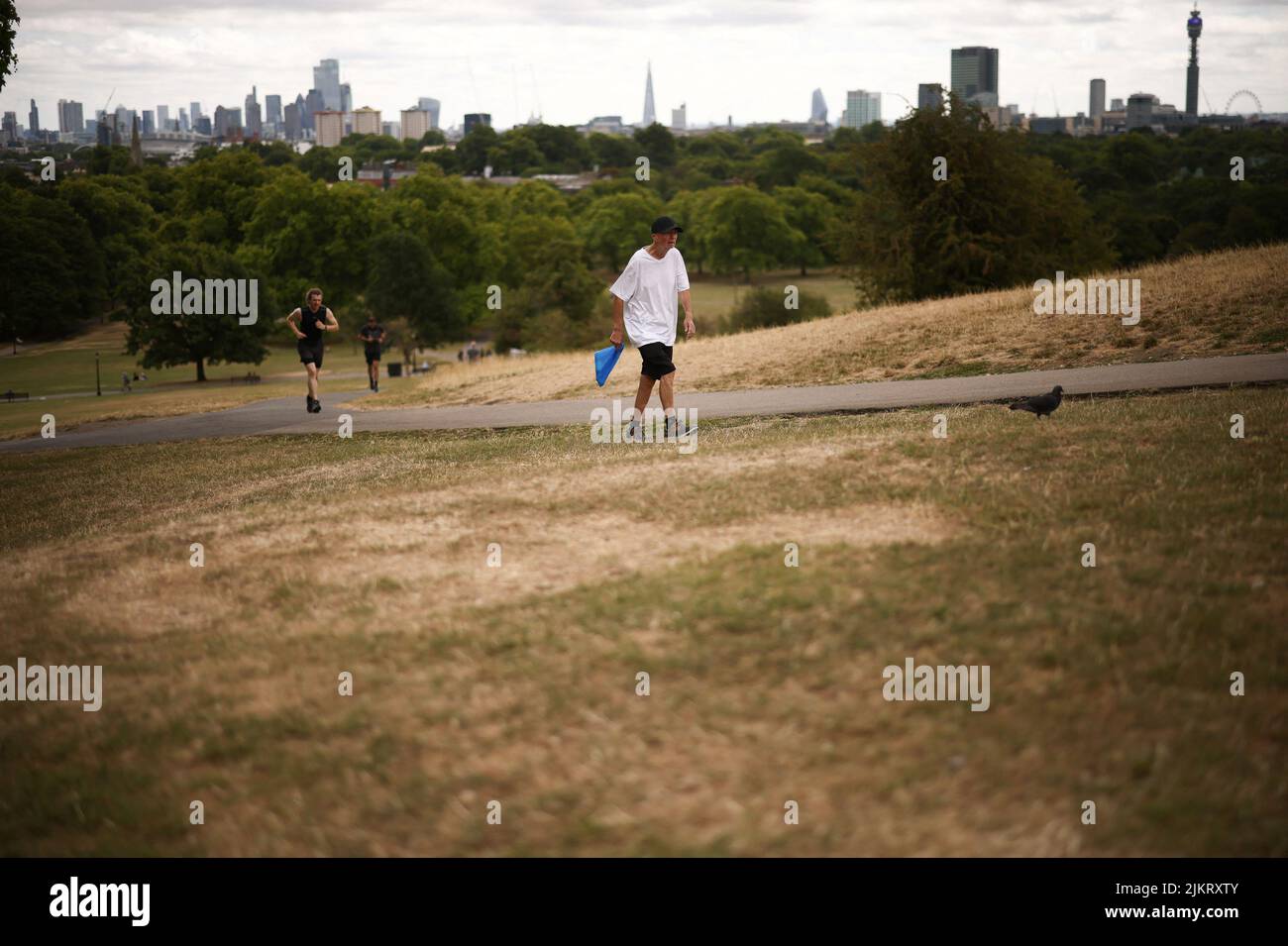 People walk past dry ground and dead grass on Primrose Hill, following a long period of hot weather and little rainfall, in London, Britain, August 3, 2022. REUTERS/Henry Nicholls Stock Photo