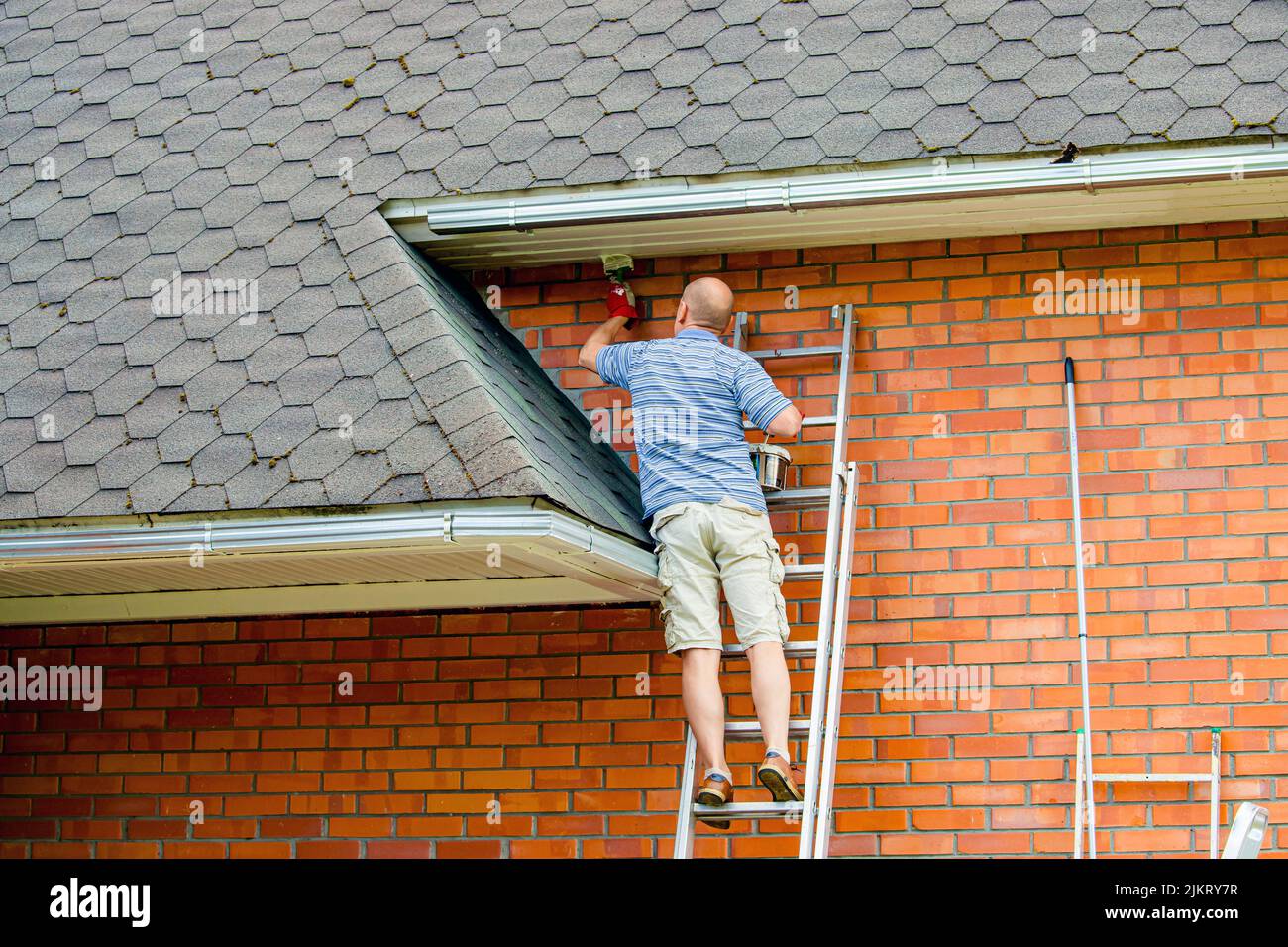 Man home owner working repainting house with paint brush and white paint outdoors in summer. Stock Photo