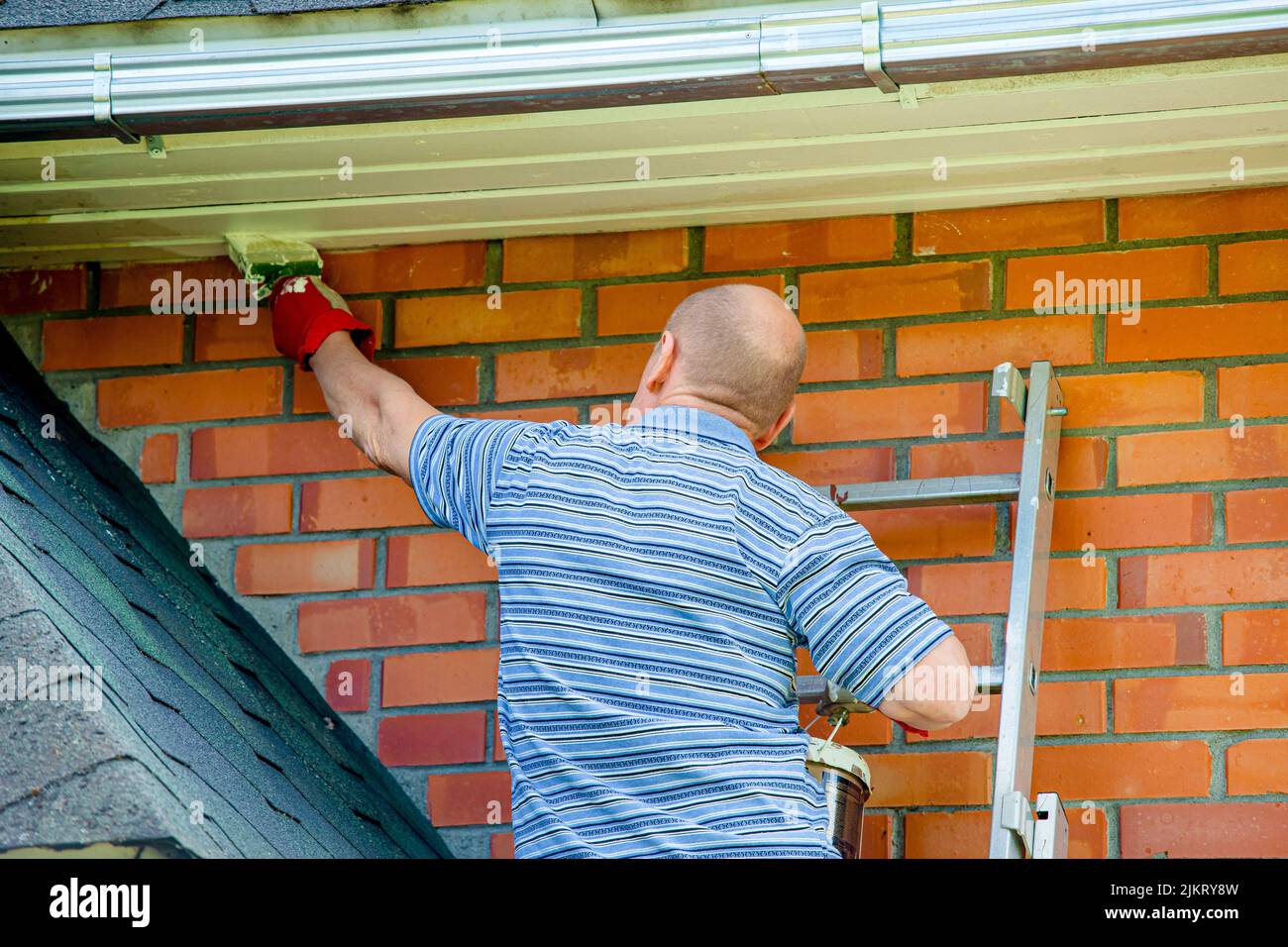 Man home owner working repainting house with paint brush and white paint outdoors in summer. Stock Photo