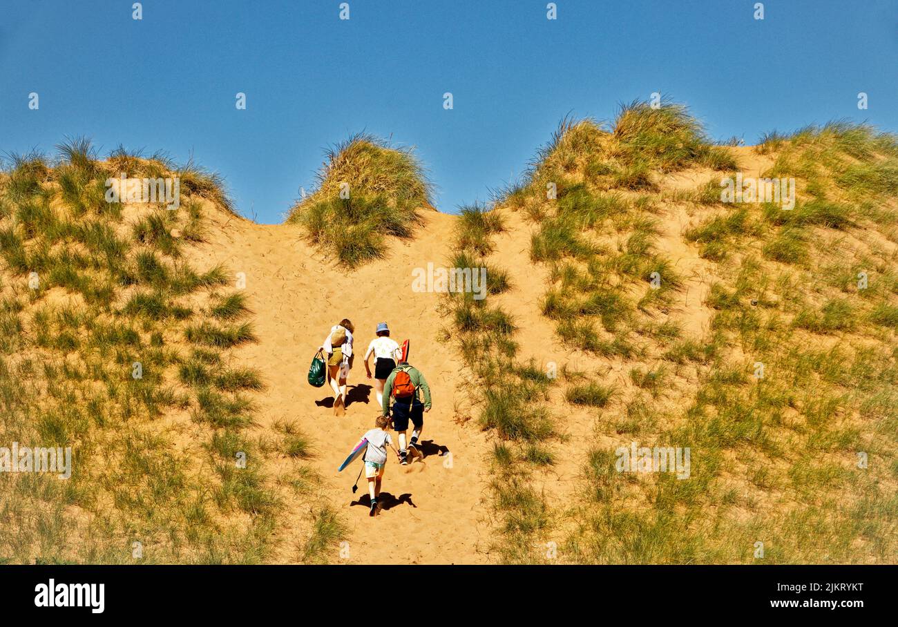 RED POINT BEACH ROSS AND CROMARTY SCOTLAND PEOPLE CLIMBING UP A LARGE RED SAND DUNE Stock Photo