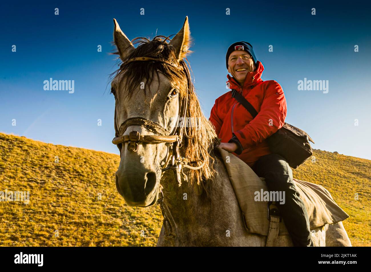 Georg Berg sits on a horse against a blue sky by the Tulpar-Kul lakes in Kyrgyzstan, the animal looking directly into the camera. Stock Photo