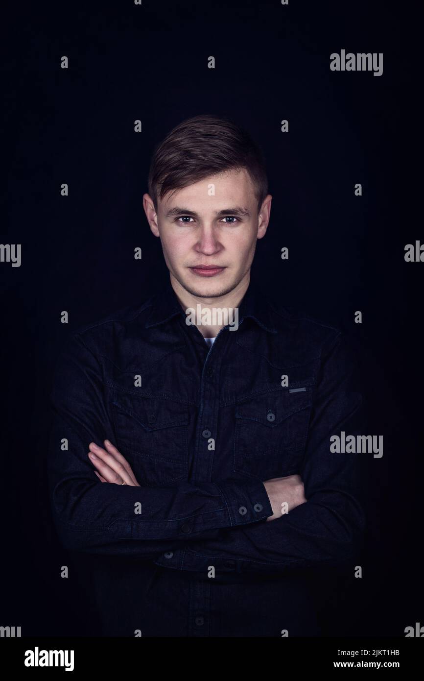 Young man hands crossed portrait isolated on dark background. Boy teenager looks confident to camera, keeps arms folded Stock Photo