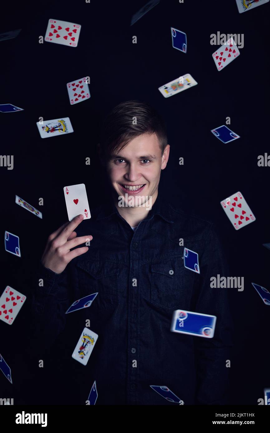 Successful young man holds up a victory lucky card. Gambler play luck games and win, isolated on dark background. Gambling jackpot winner with an ace Stock Photo