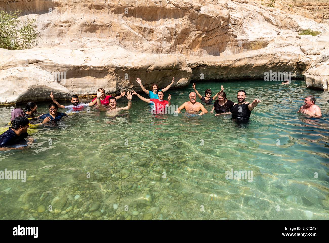 Wadi Bani Khalid, Oman - February 12, 2020: Happy tourists enjoying the crystal water lake of the Wadi Bani Khalid oasis in the desert in Sultanate of Stock Photo