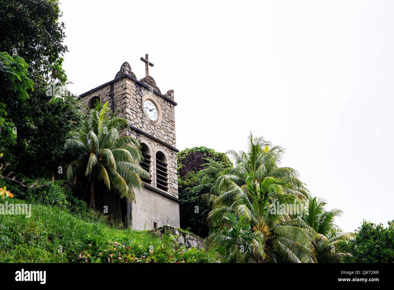 Stone Clock Tower (Tour de l'Horloge) on the hill next to the Immaculate Conception Cathedral, old building with clock and Holy Cross, Victoria, Mahe Stock Photo