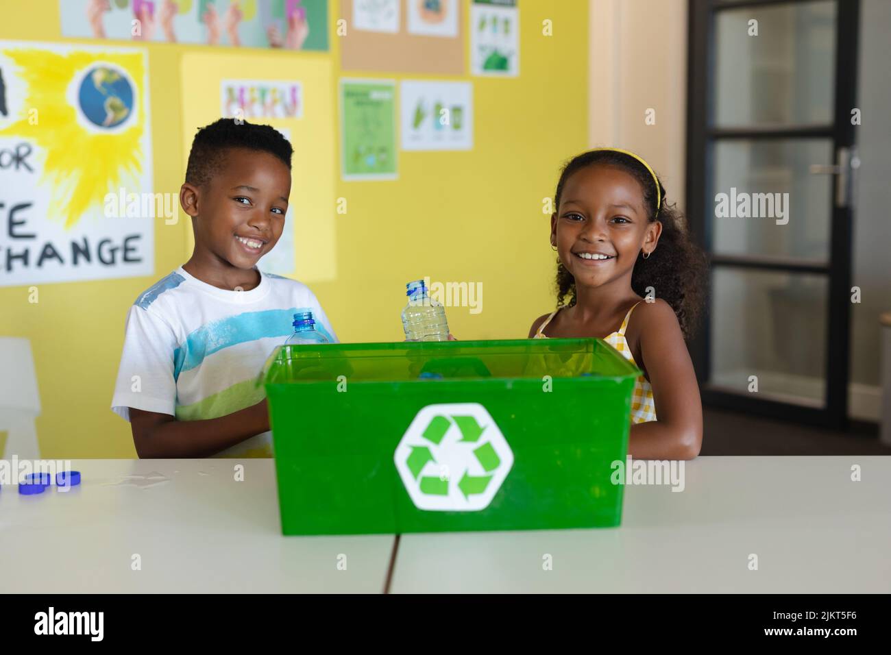 Portrait of smiling african american elementary students with recycling container at desk in school Stock Photo