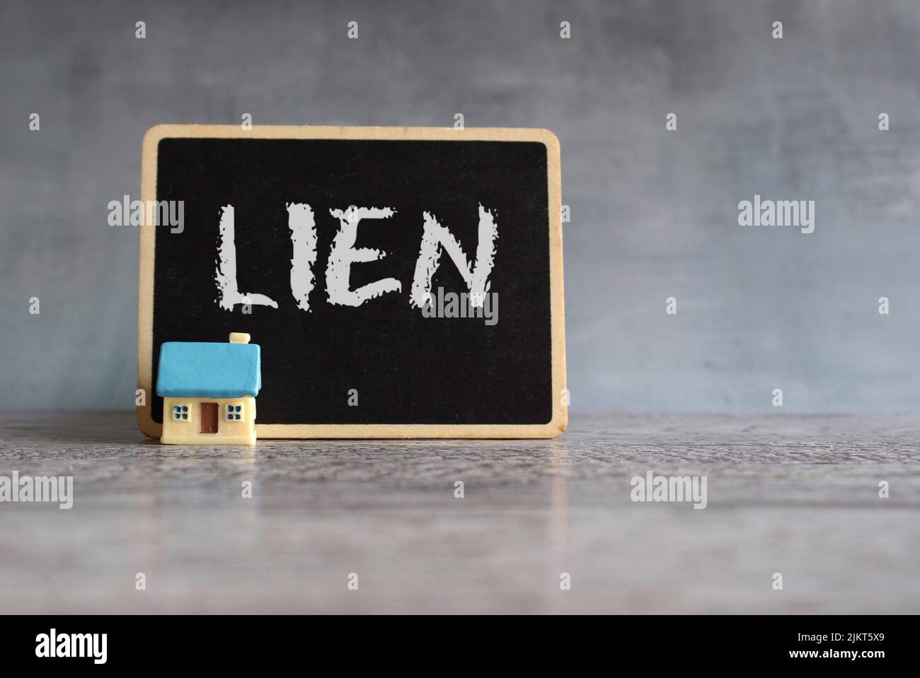Toy house and chalkboard with text LIEN. Property and real estate