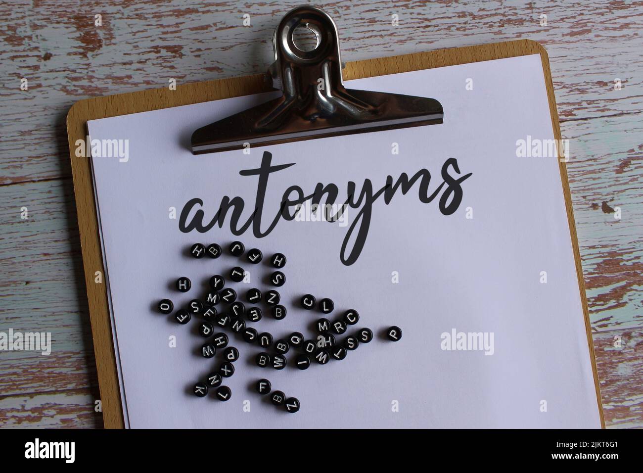 Top view image of paper clipboard with text antonyms and alphabet beads. Stock Photo