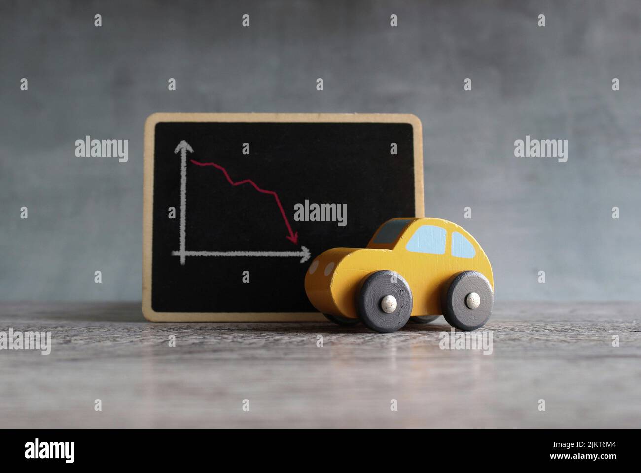 Toy car and chalkboard with downward arrow graph. Car rental dealer