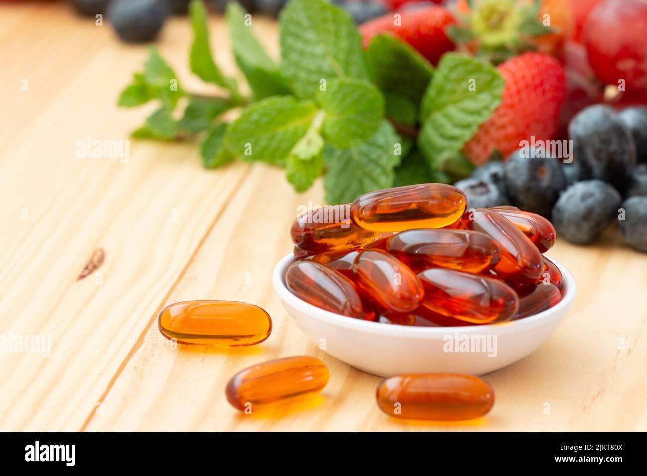 Lecithin gel vitamin supplement capsules  in a small cup on the wooden table with variety fruit. Stock Photo