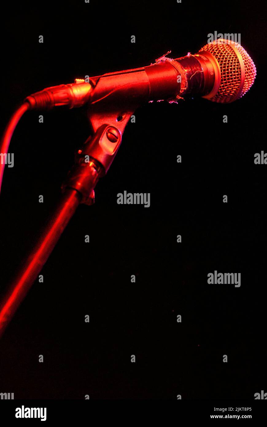 A closeup shot of a used stage microphone set up on a stand under red lights and black background Stock Photo