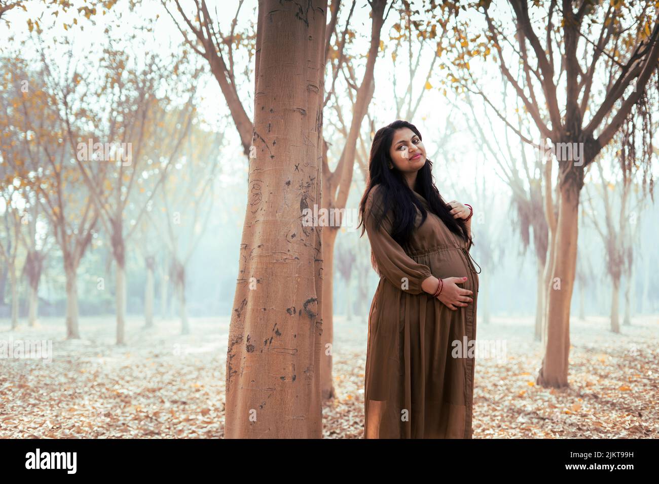 A young beautiful pregnant female posing holding her belly in a park Stock Photo
