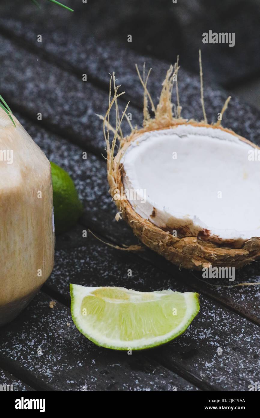 A vertical shot of open coconut fruit with clean white meat and fresh lime on a dark surface Stock Photo