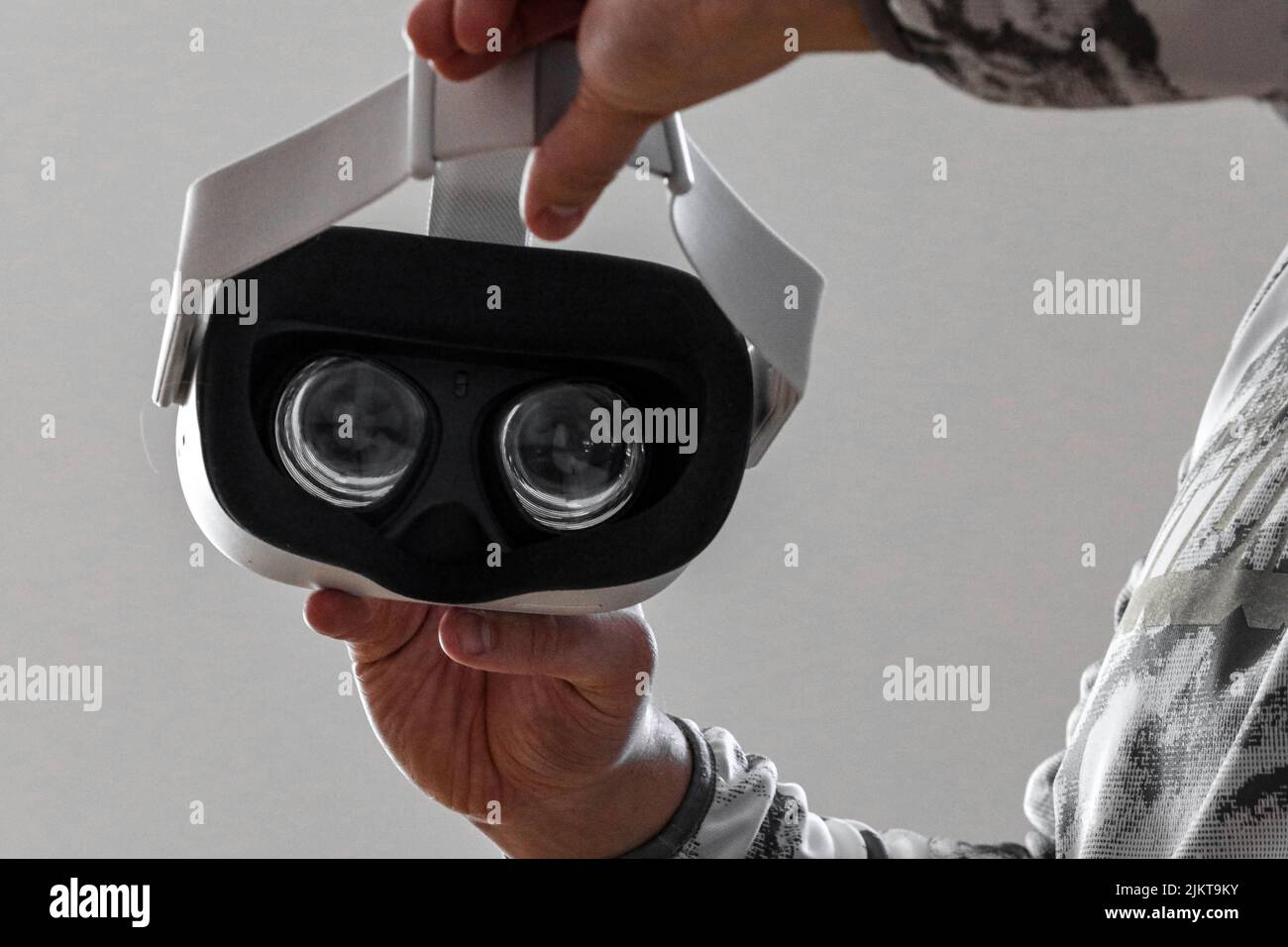 A man holding a virtual reality headset against a white wall background Stock Photo