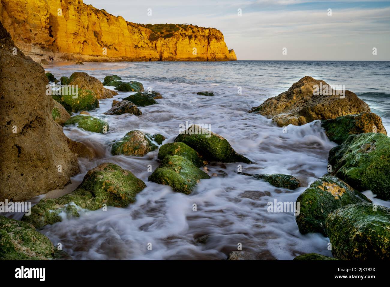 A Mossy stones on the seashore at cloudy orange sunset Stock Photo