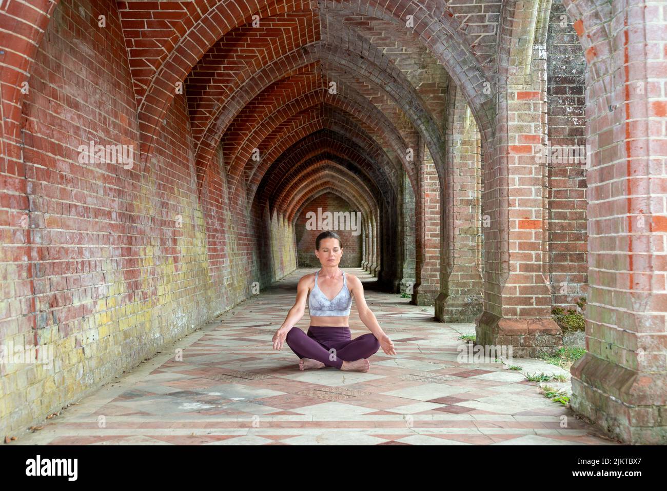 Sporty woman practicing yoga and meditating. Brick arches background. Stock Photo
