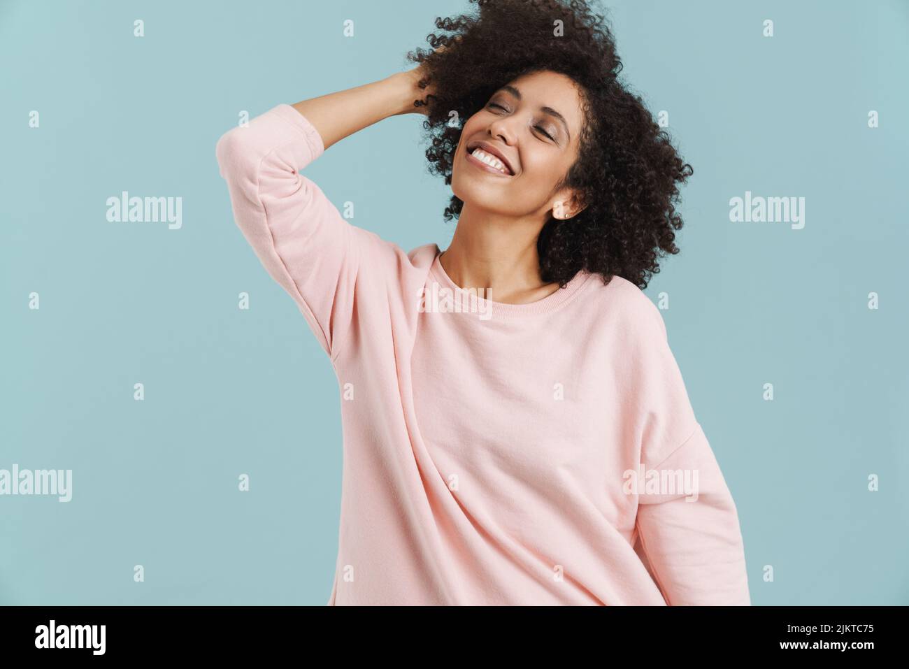 Young black woman with curly hair smiling and holding her head isolated ...