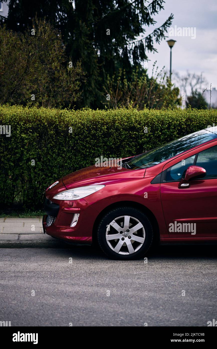 A vertical shot of a parked red Peugeot 308 car by a sidewalk. Stock Photo