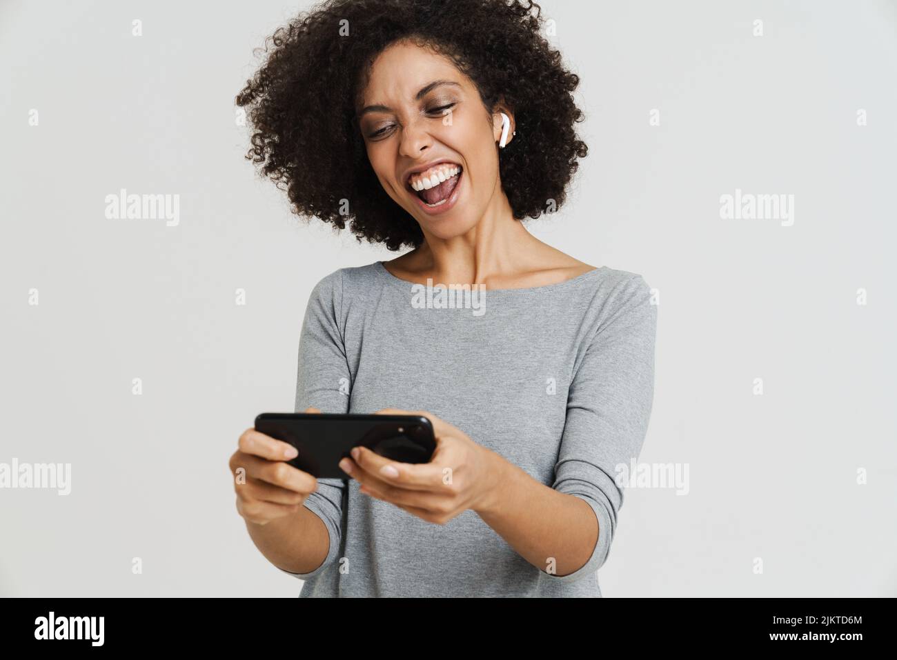 Young black woman in earphones smiling and using mobile phone isolated over white background Stock Photo