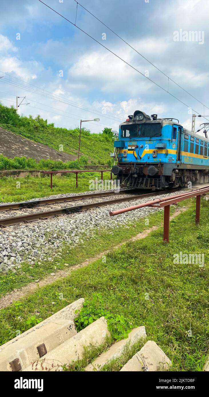 A vertical shot of a blue locomotive driving on the railroad surrounded ...