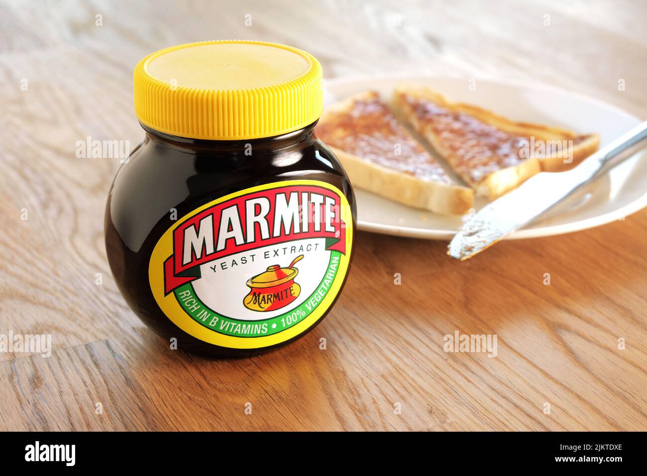 April 22nd, 2015: Jar of Marmite, unopened on wooden table top. Slice of toast on a white plate in background. Stock Photo