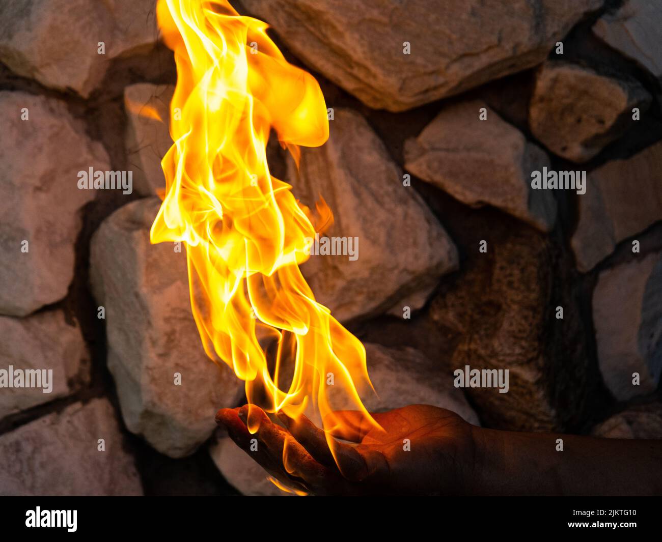 A closeup of the burning flames of fire on top of the man's hand holding near the brick wall Stock Photo