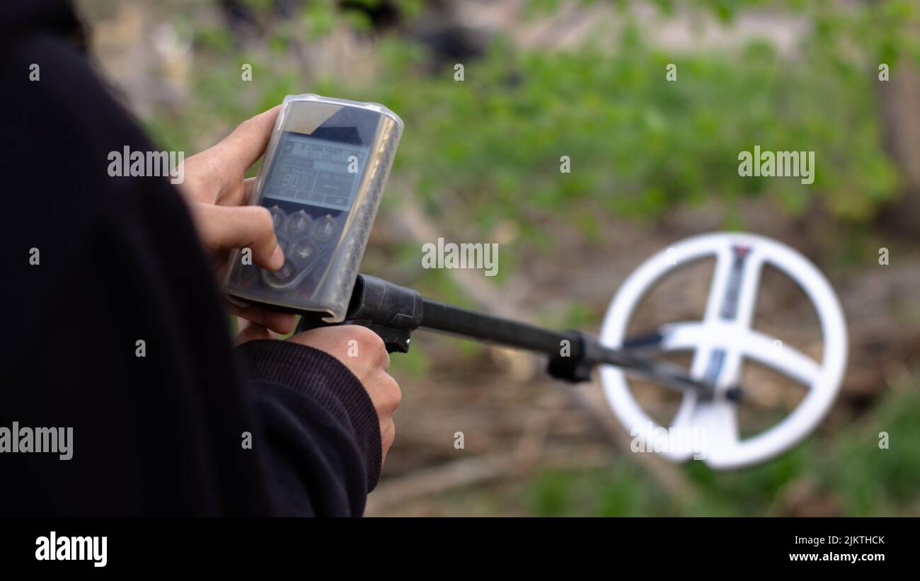 A man sets up a wireless metal detector to search for treasures underground.  Metal detector coil out of focus Stock Photo
