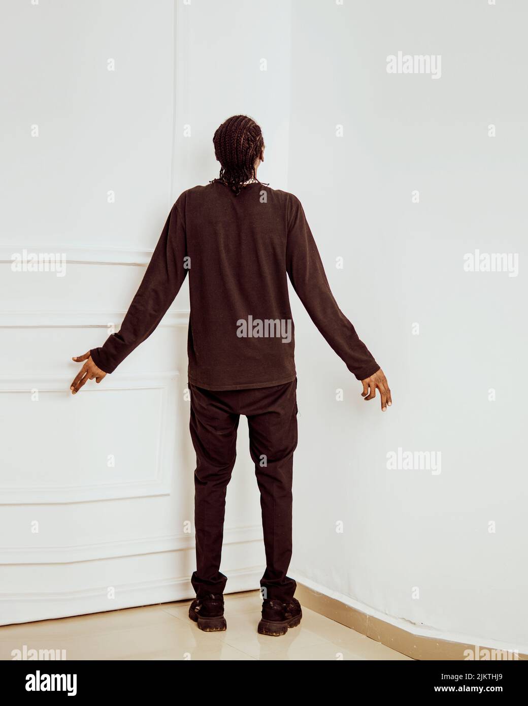 A vertical shot of a male standing in the corner of the room and looking at the white walls Stock Photo