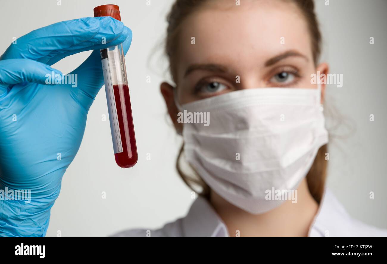 young woman with medical face mask and medical gloves is handling a blood test tube Stock Photo
