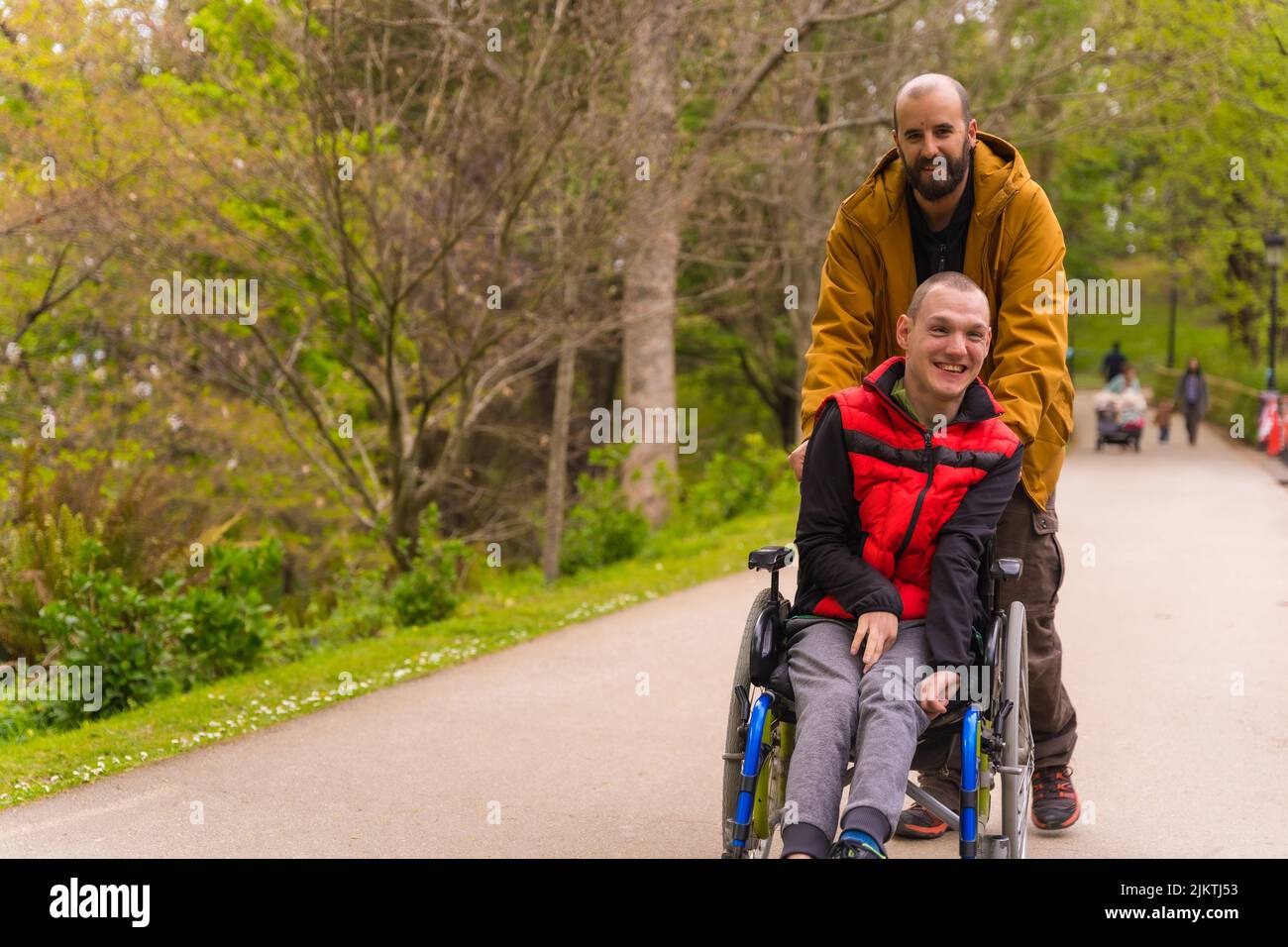 Paralyzed young man in the wheelchair being pushed by a friend in a ...