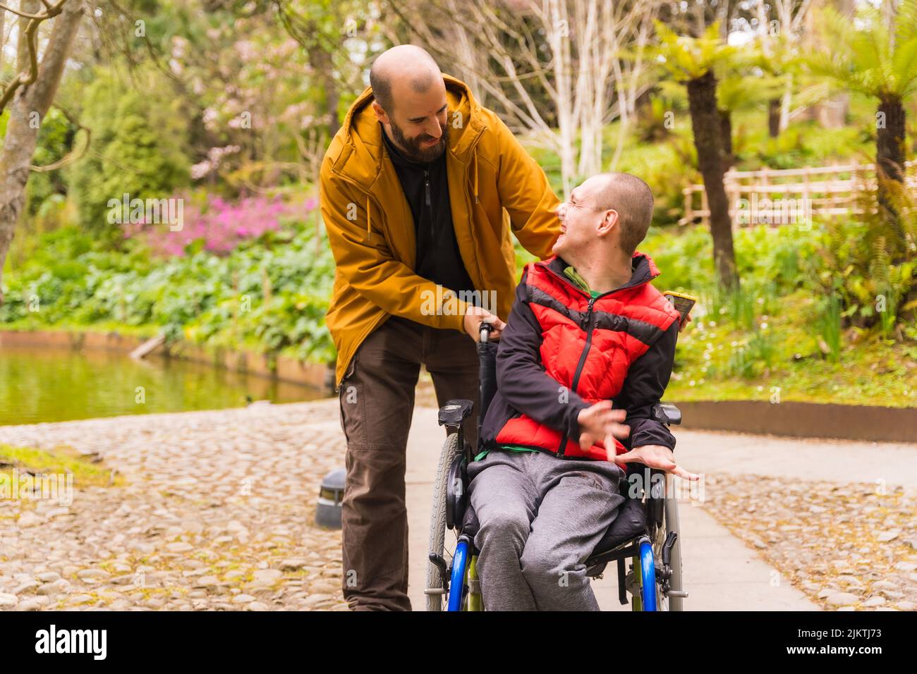 Paralyzed young man in the wheelchair being pushed by a friend in a ...