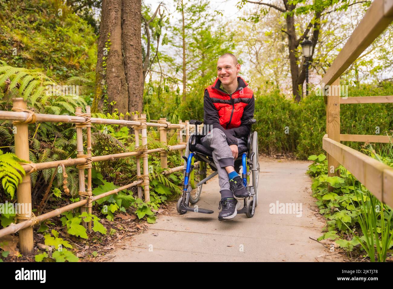 Portrait of a paralyzed young man in a public park in the city. Sitting ...