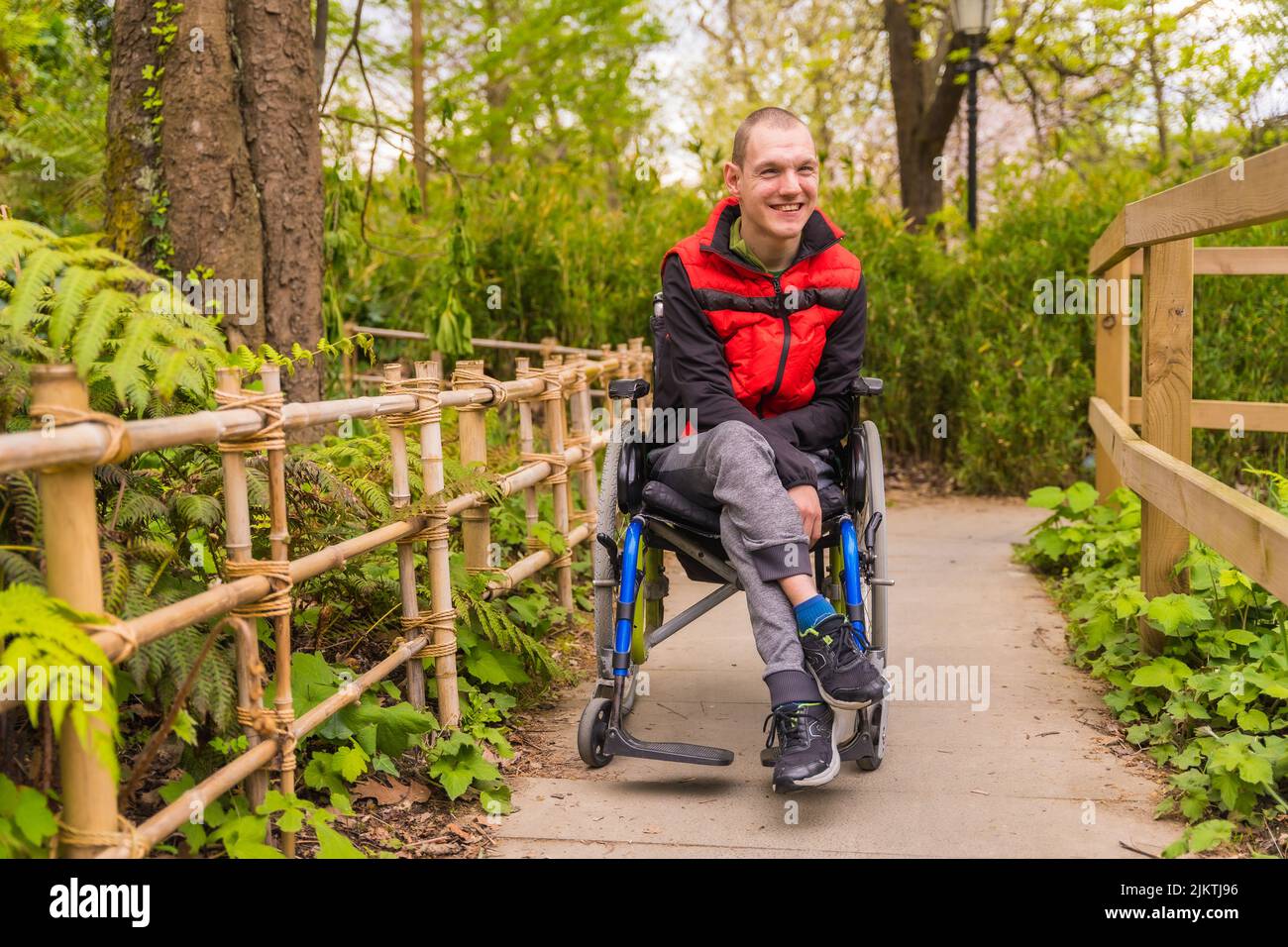 Portrait of a paralyzed young man in a public park in the city. Sitting ...