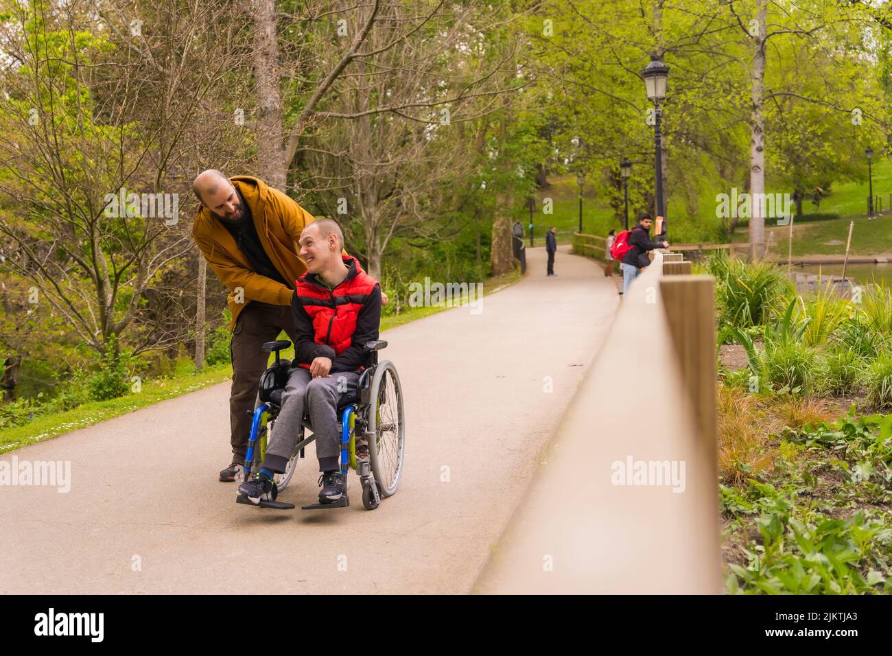 Paralyzed young man in a wheelchair being pushed by a friend in a ...