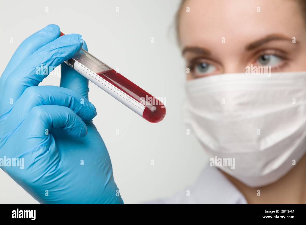 young woman with medical face mask and medical gloves is handling a blood test tube Stock Photo