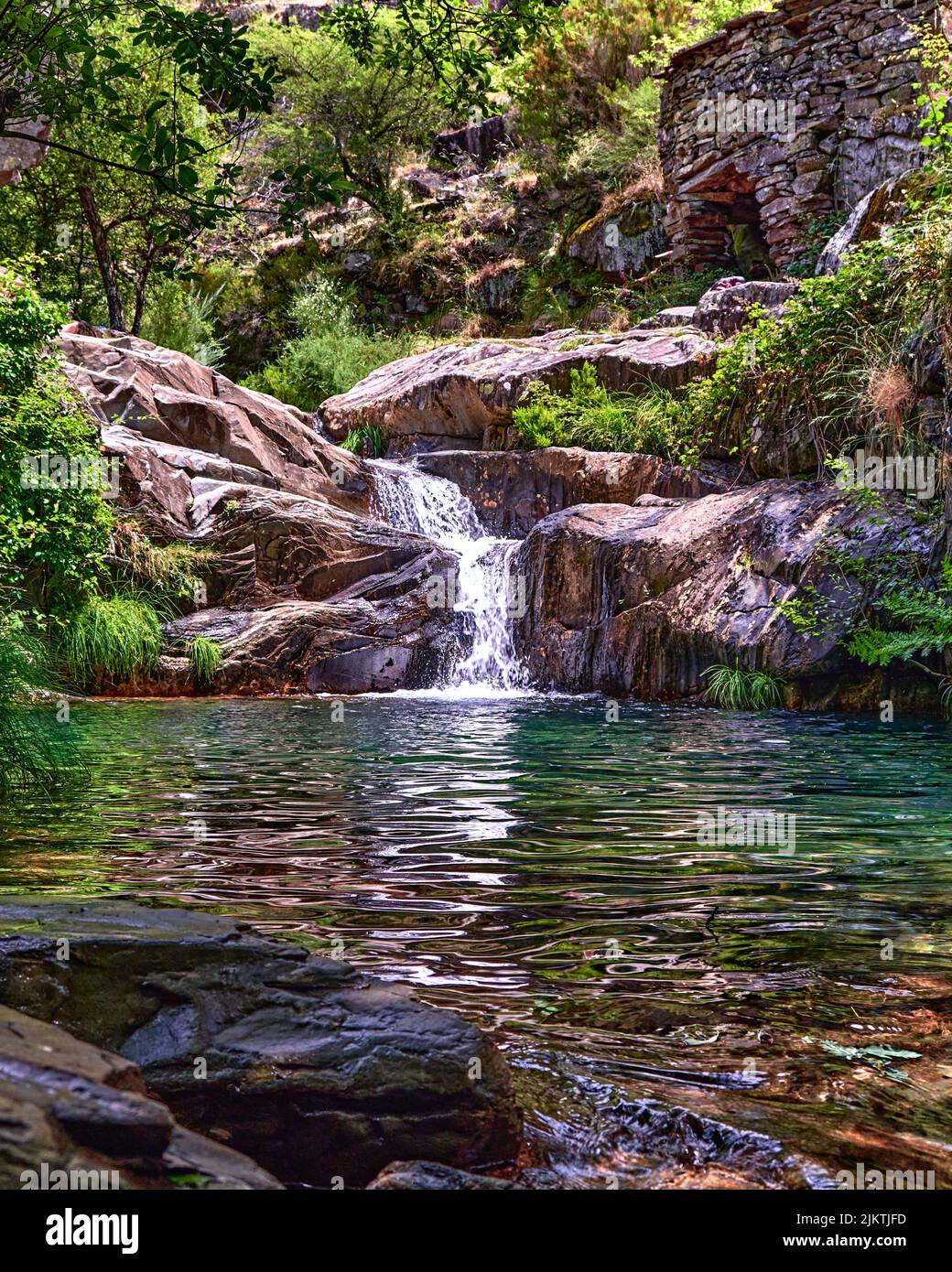 A vertical shot of a small waterfall merging into the Paiva river in the Arouca Geopark on a sunny day Stock Photo