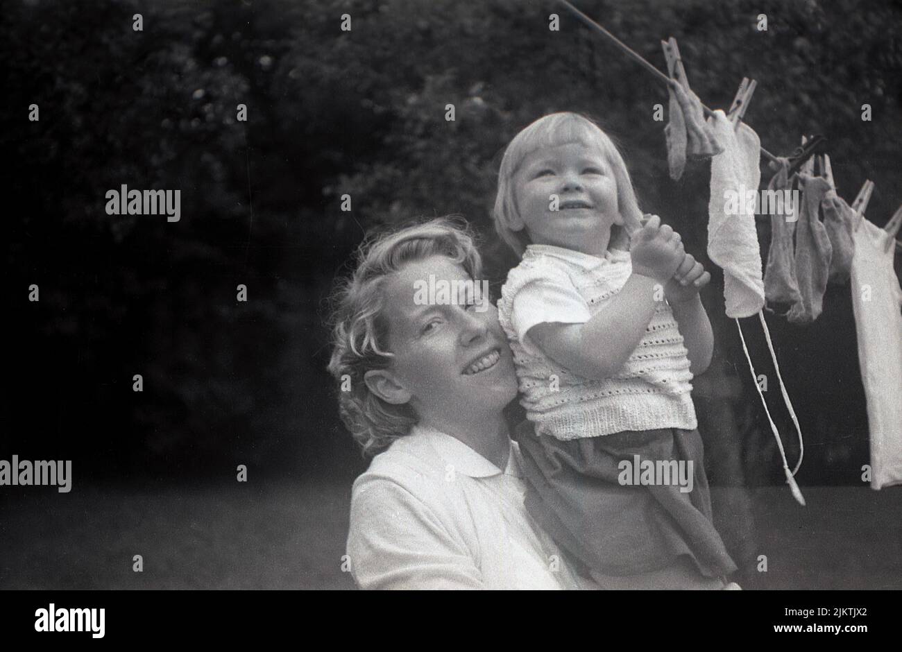 1960s, historical, a mother holding her young daughter up, whose helping to put the washing on the clothes line, England, UK. Stock Photo