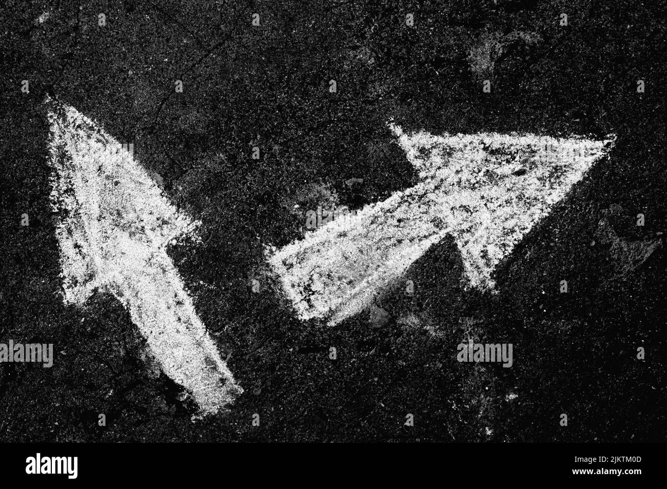 Two arrows pointing to different directions drawn on a black surface with chalk Stock Photo