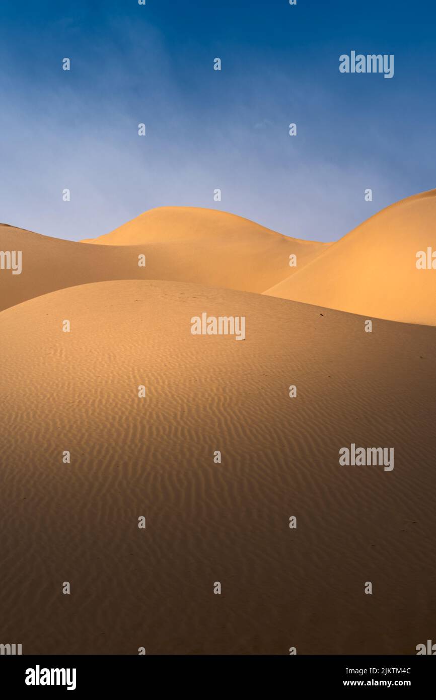 A vertical shot of the dunes in the desert against the background of blue sky. Stock Photo