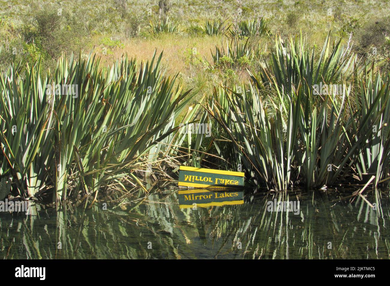 The box on the shore with the name Mirror Lakes reflecting on the water surface. New Zealand. Stock Photo